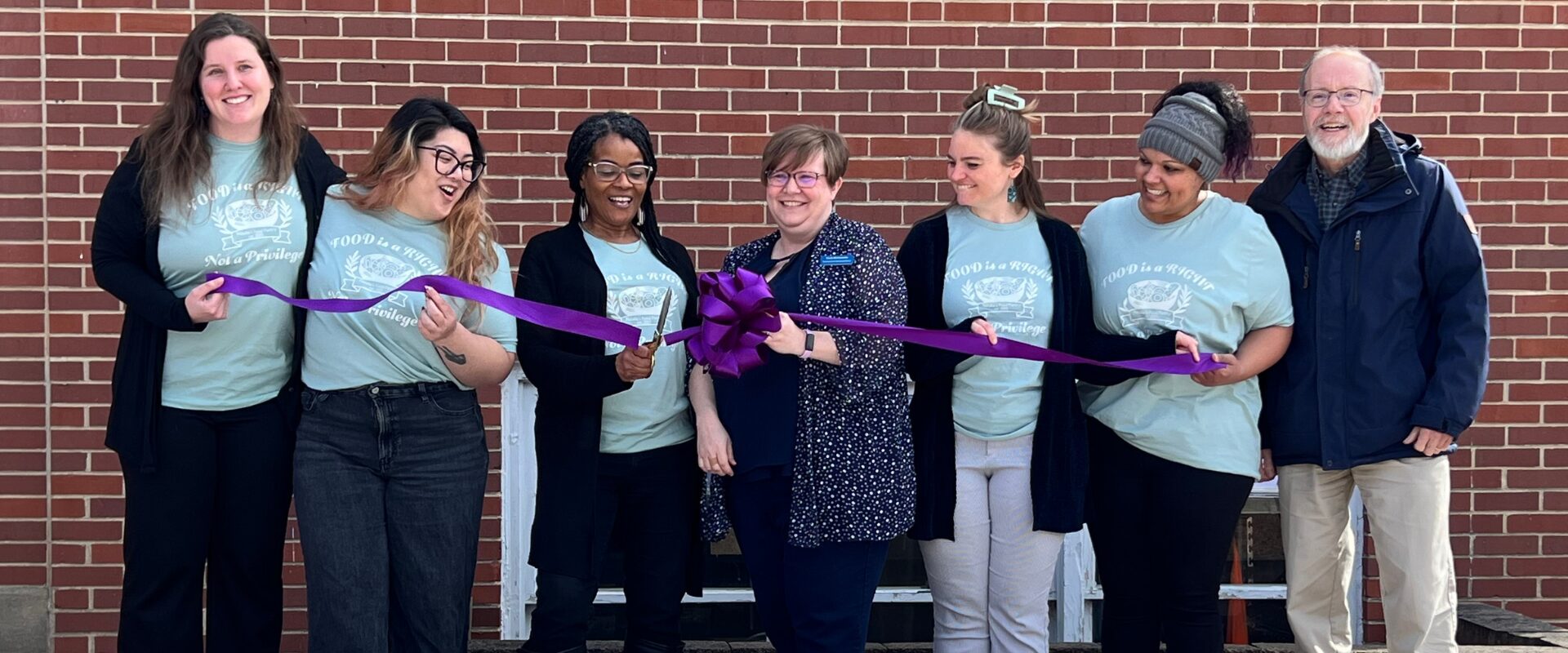 Happy people holding a purple ribbon that is being cut in half with scissors