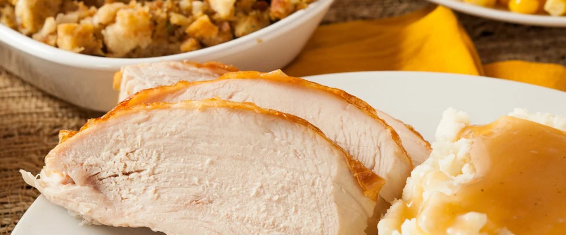 Turkey slices, mashed potatoes and gravy on a plate with stuffing in a nearby bowl